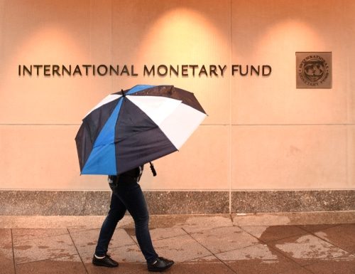 Un passant marche sous son parapluie devant la façade du Fonds monétaire international
